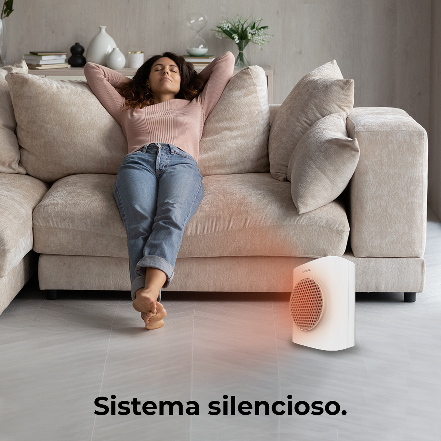 Mujer relajándose en un sofá. Un calefactor blanco en el suelo. La escena es en una sala de estar. El texto abajo dice 'sistema silencioso'.