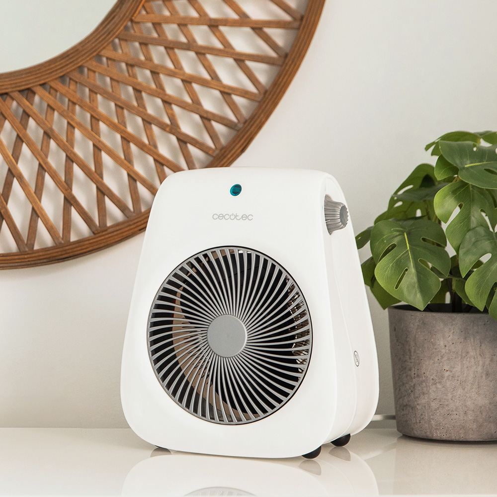 Un calefactor Cecotec blanco sobre una superficie blanca. Un espejo decorativo de madera detrás. Una planta en maceta a la derecha.