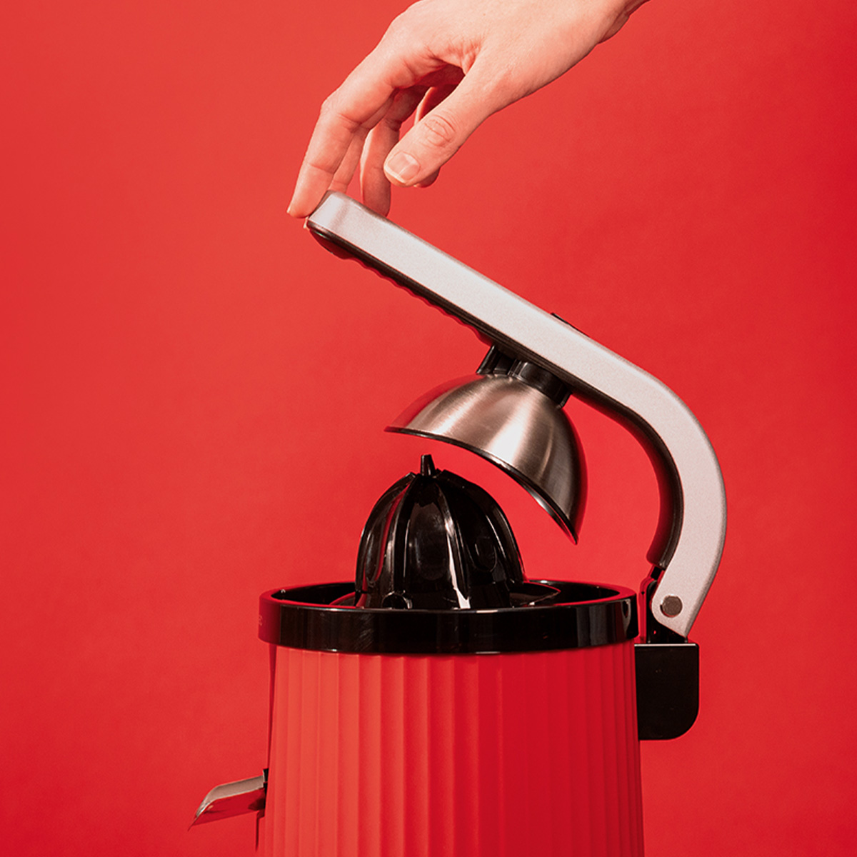 Una mano colocando la parte superior de un exprimidor de cítricos rojo y plateado. El fondo es rojo.