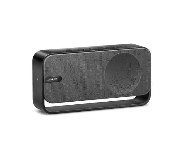 Un altavoz Bose negro sobre fondo blanco. Tiene forma rectangular redondeada con rejilla de altavoz y botones en la parte superior.