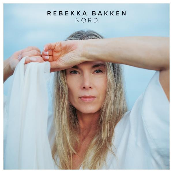 Frau mit blonden Haaren, trägt Weiß, hält Stoff. Text oben: 'Rebekka Bakken Nord'. Blauer Himmel im Hintergrund.
