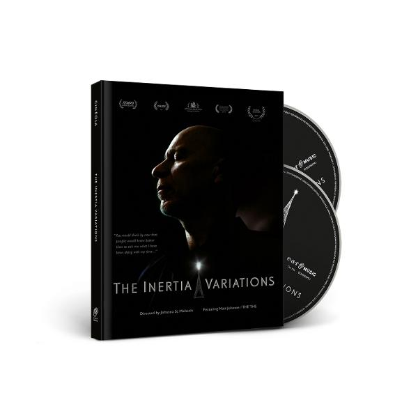 Das Bild zeigt eine DVD-Hülle mit dem Gesicht eines Mannes darauf. Zwei CDs liegen daneben. Der Text lautet 'The Inertia Variations'.