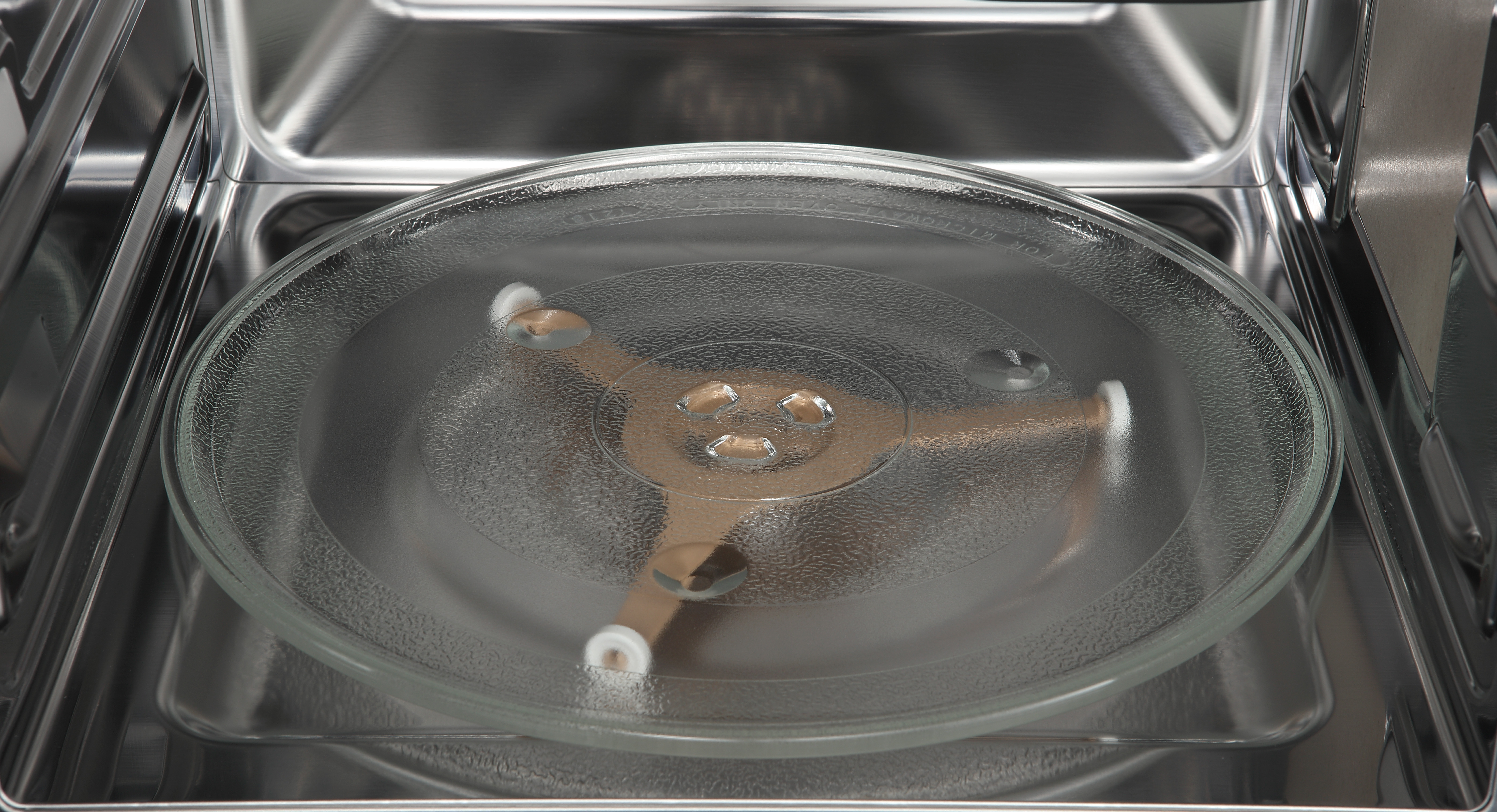 Wewnątrz kuchenki mikrofalowej. Szklany talerz spoczywa na obrotowej podstawie. Ściany są stalowe.