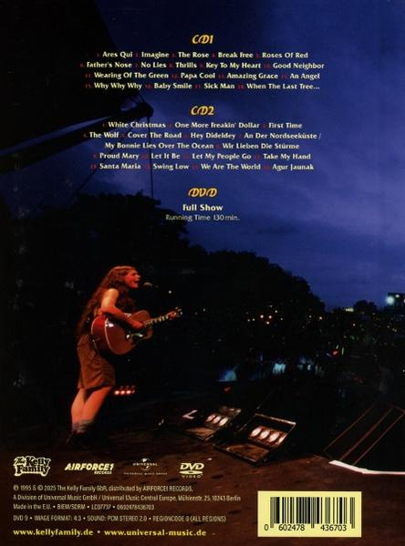 Eine Frau singt und spielt Gitarre auf der Bühne. Im Hintergrund sind Songlisten und DVD-Infos.