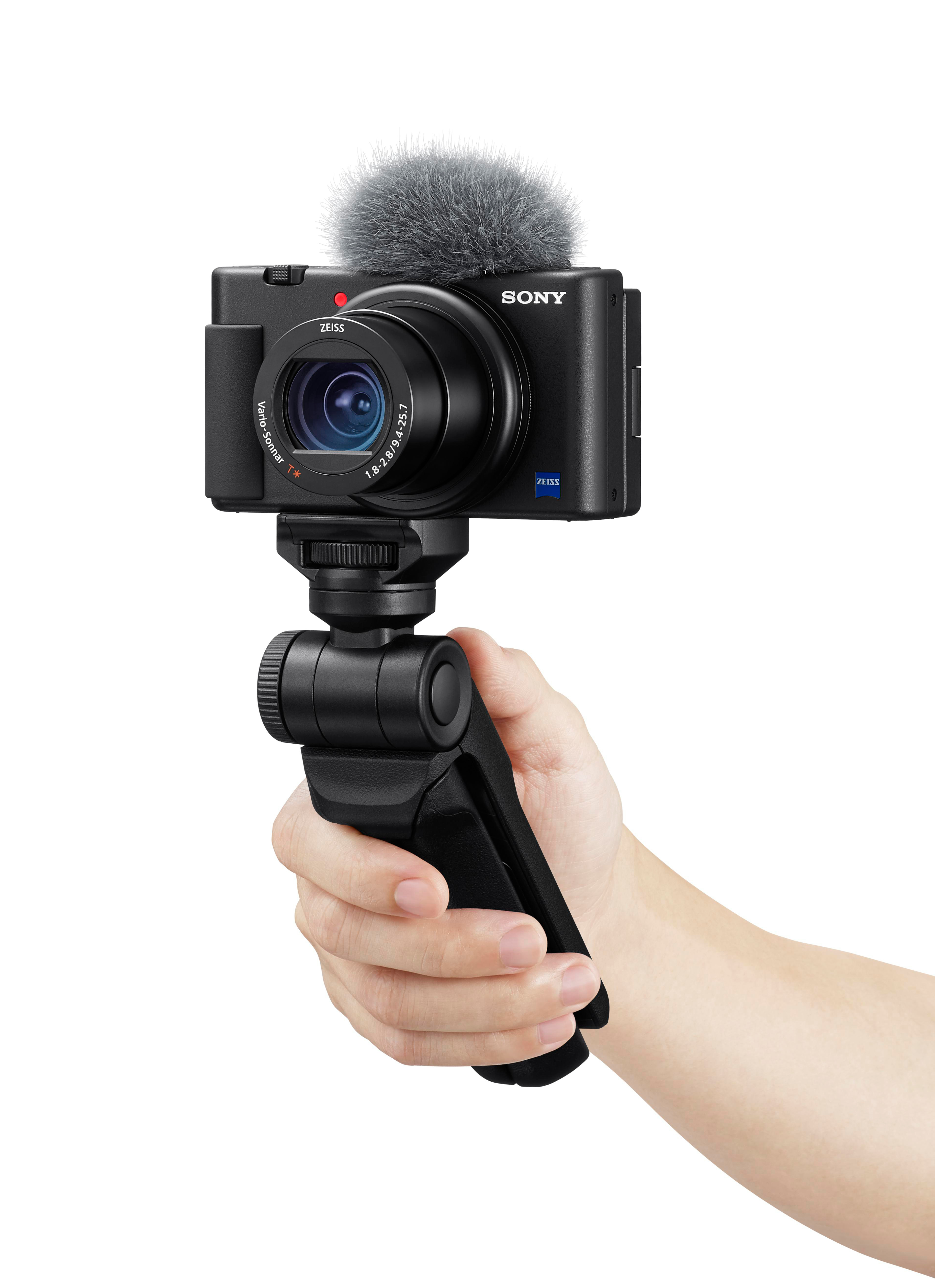Eine schwarze Sony-Kamera mit Mikrofon wird von einer Hand gehalten. Die Kamera ist auf einem kleinen Stativ montiert.