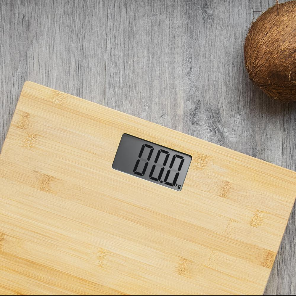 Una báscula de madera que muestra 0,0 kg, con un coco sobre una superficie de madera gris. La báscula está enfocada.
