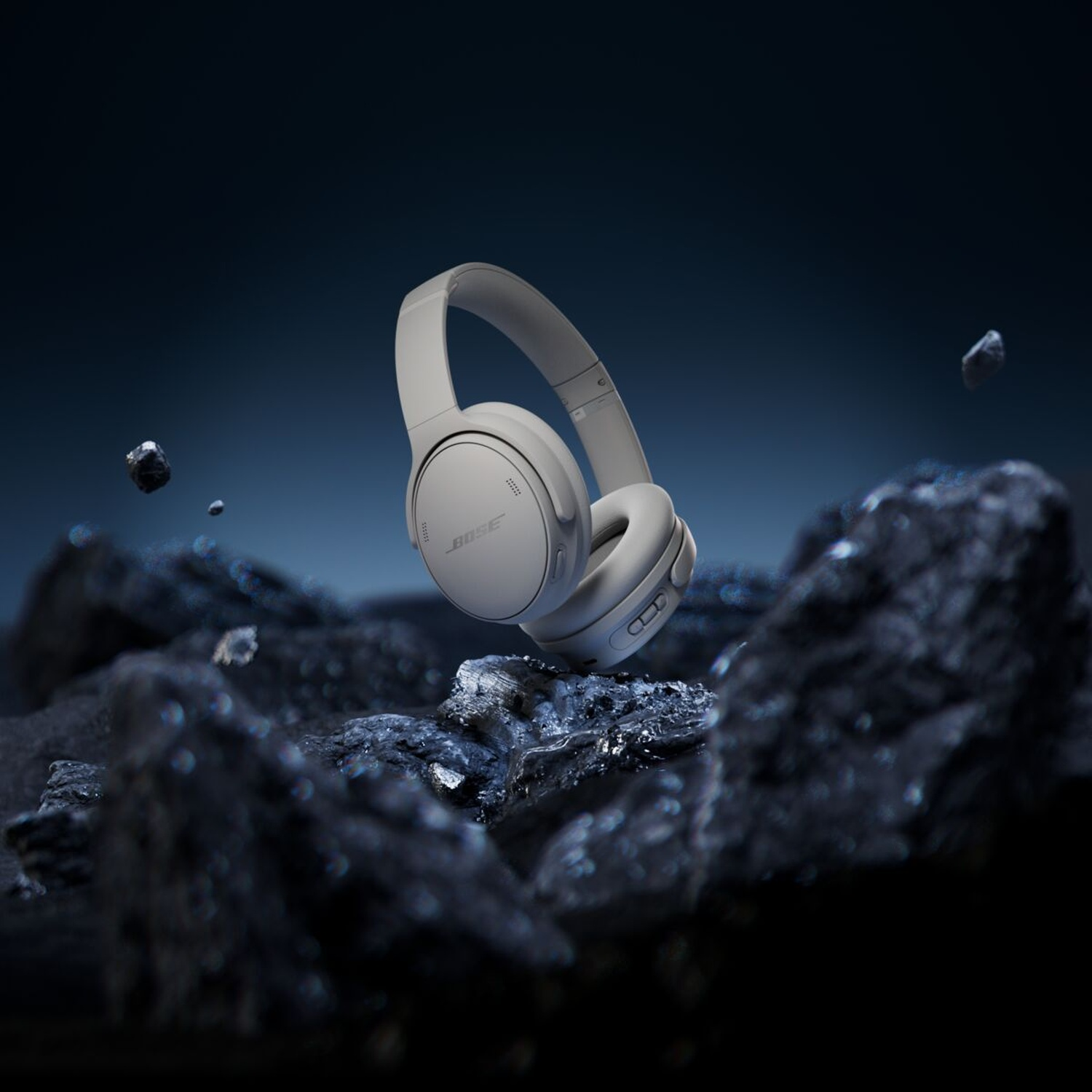 Gray headphones floating above dark rocks against a dark blue background. The Bose logo is visible on the headphones.