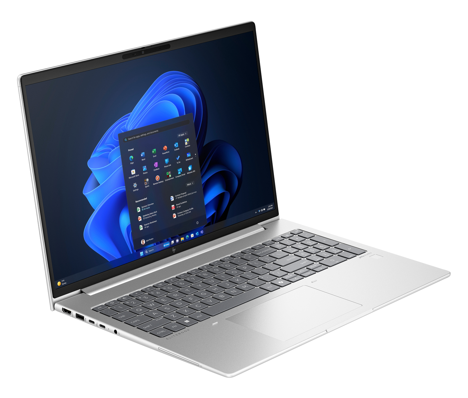 Una laptop plateada está abierta, mostrando la interfaz de Windows 11. La pantalla muestra el menú de inicio e iconos de aplicaciones. El teclado es visible.