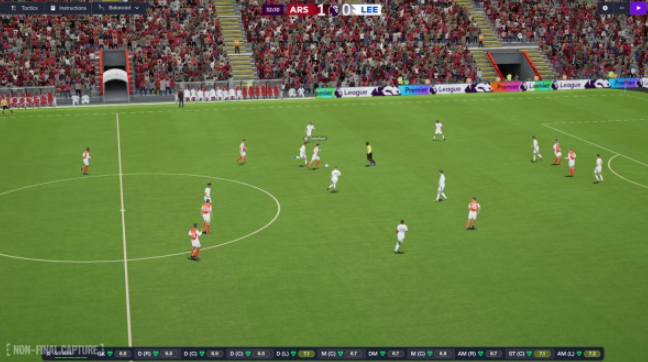 Ein Fußballspiel im Gange. Spieler in weißen und orangefarbenen Trikots auf einem grünen Feld. Zuschauer sind auf der Tribüne.