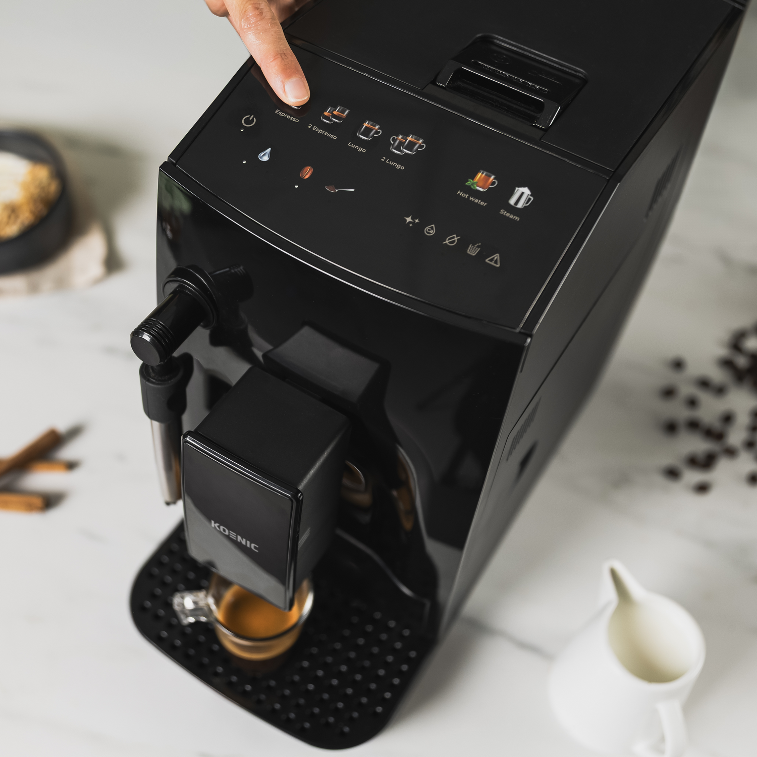 Una mano presiona el botón de espresso en una máquina de café negra. Una taza se está llenando, con granos, azúcar y un recipiente de crema cerca.