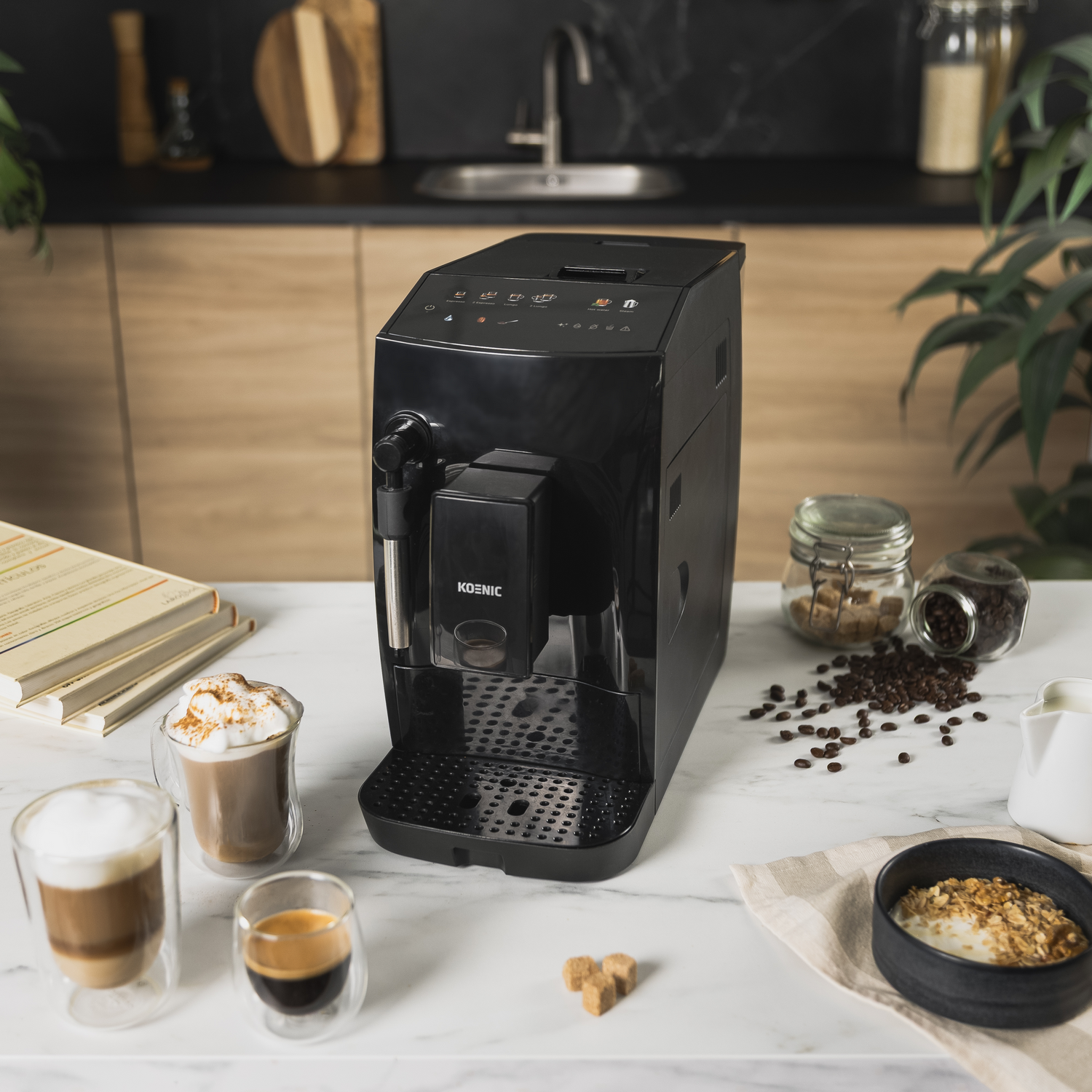 Una cafetera negra con bebidas de café, granos de café, cubos de azúcar y un cuenco de granola sobre una superficie de mármol.