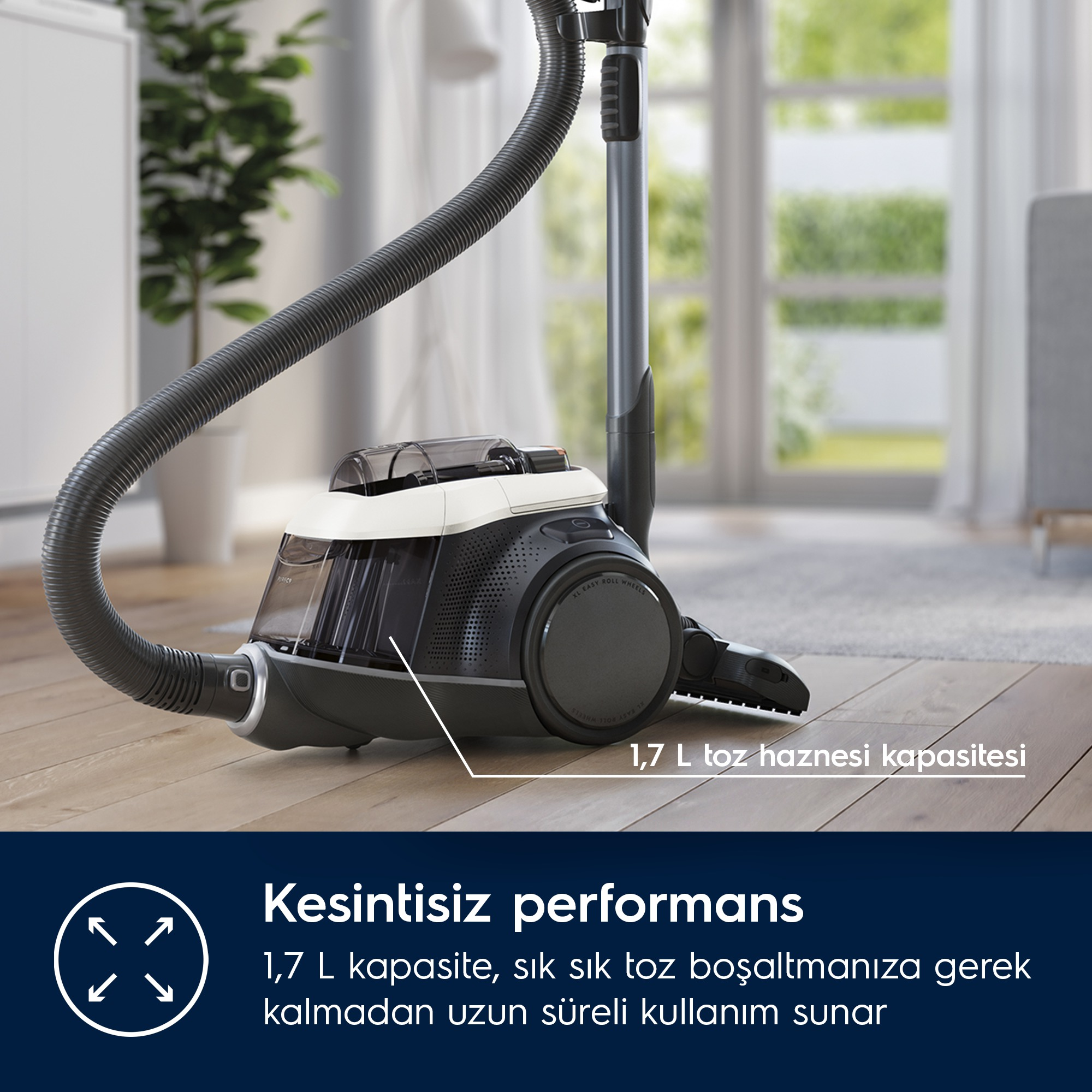 Ahşap zeminde, uzun hortumlu ve 1,7 L kapasiteli siyah beyaz bir elektrikli süpürge.