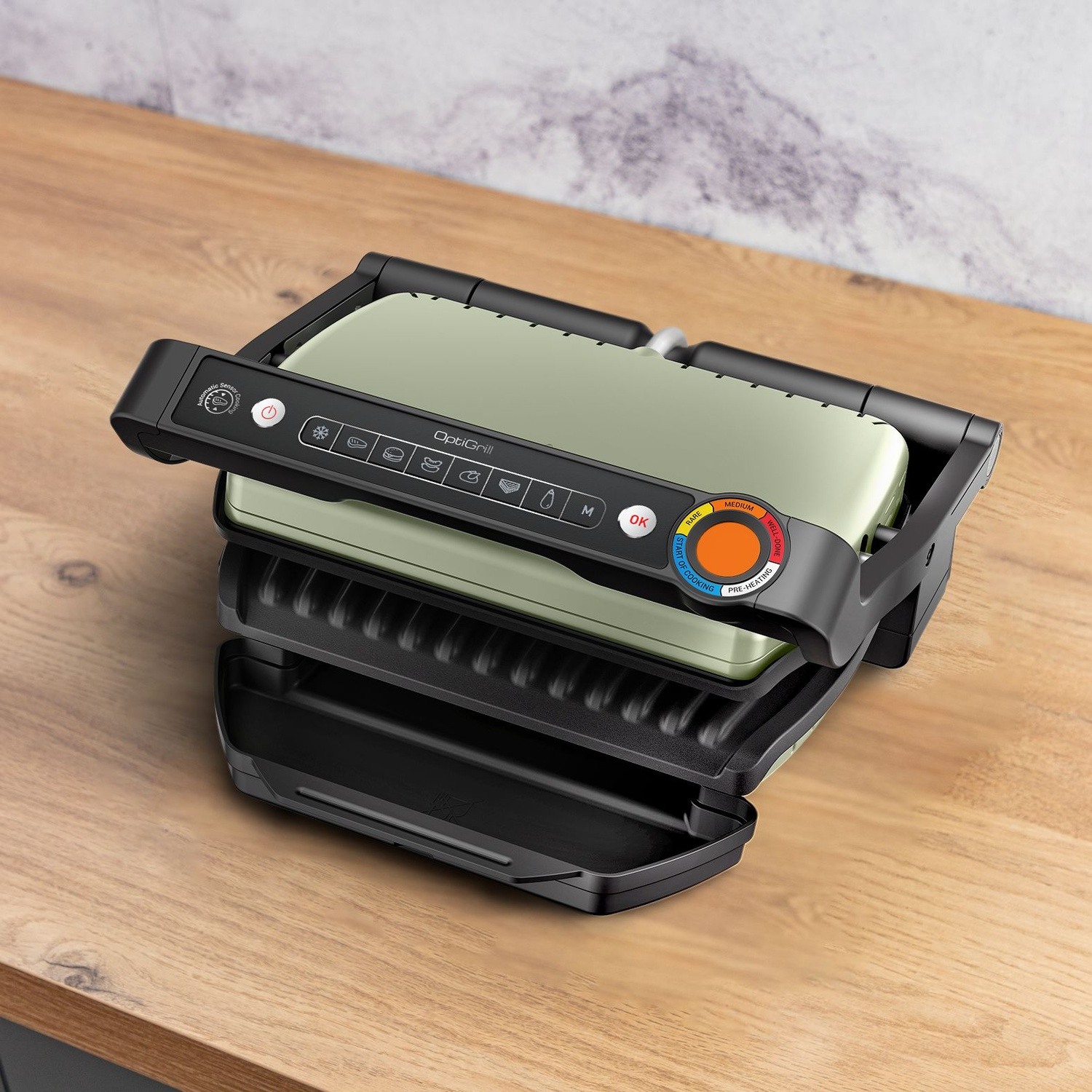 Un grill électrique OptiGrill sur une surface en bois. Il est noir et vert, avec un panneau de contrôle. Le grill est ouvert, prêt à l'emploi.