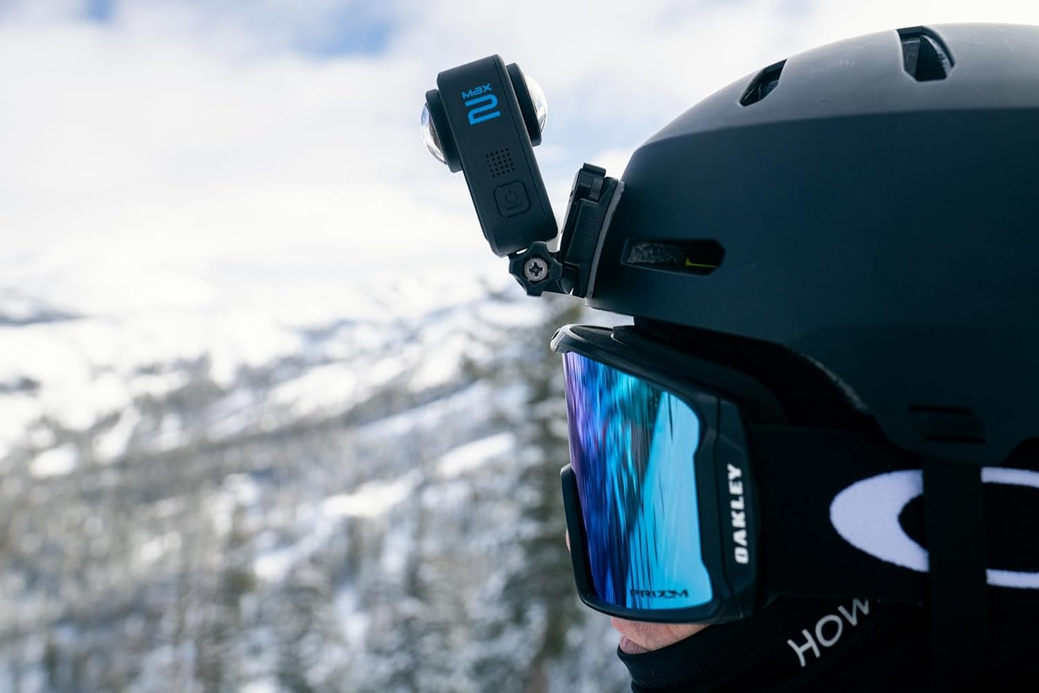 Una persona con casco negro con cámara, gafas azules y montañas nevadas de fondo.