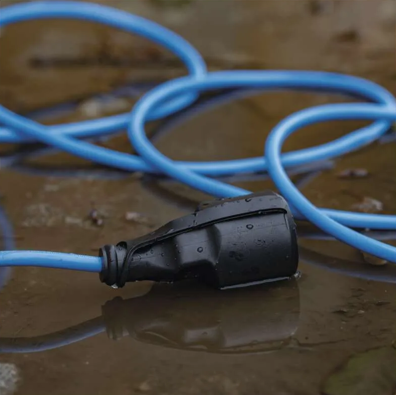 Egy fekete elektromos csatlakozó nedves talajon fekszik, kék kábellel. A kábel a csatlakozó körül kanyarodik, tükröződve a vízben.