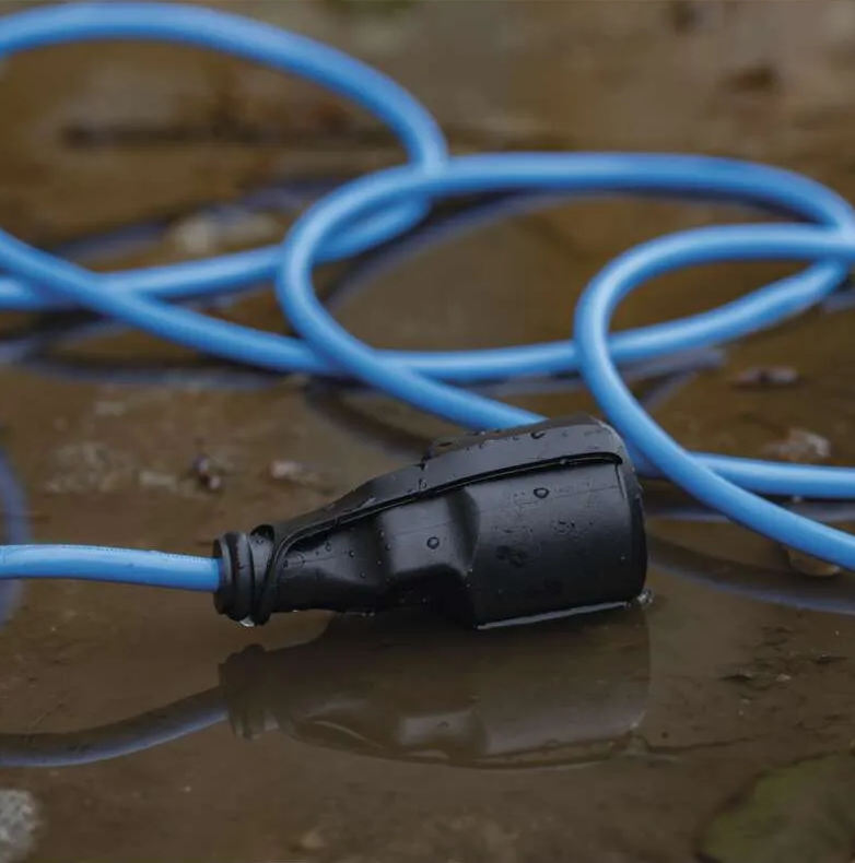 Egy fekete elektromos dugó vízben fekszik, kék kábelhez csatlakoztatva. A kábel tekercselt, és a víz tükrözi a dugót és a kábelt.