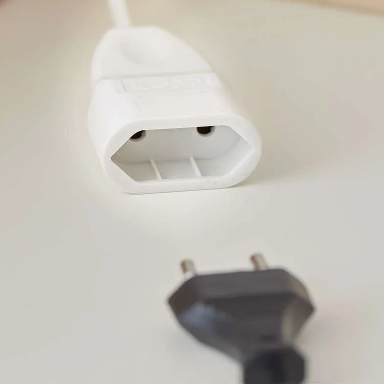 Egy fehér konnektor egy fekete dugó felett. Mindkettő fehér felületen van. A konnektor egy fehér kábelhez csatlakozik.