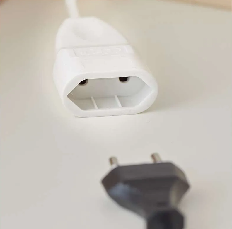 Egy fehér konnektor felül, egy fekete dugó alul, mindkettő fehér felületen. A konnektoron két lyuk van.