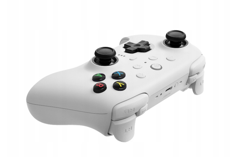 Biały kontroler do gier z czarnymi joystickami, kolorowymi przyciskami i spustami. Tło jest białe.