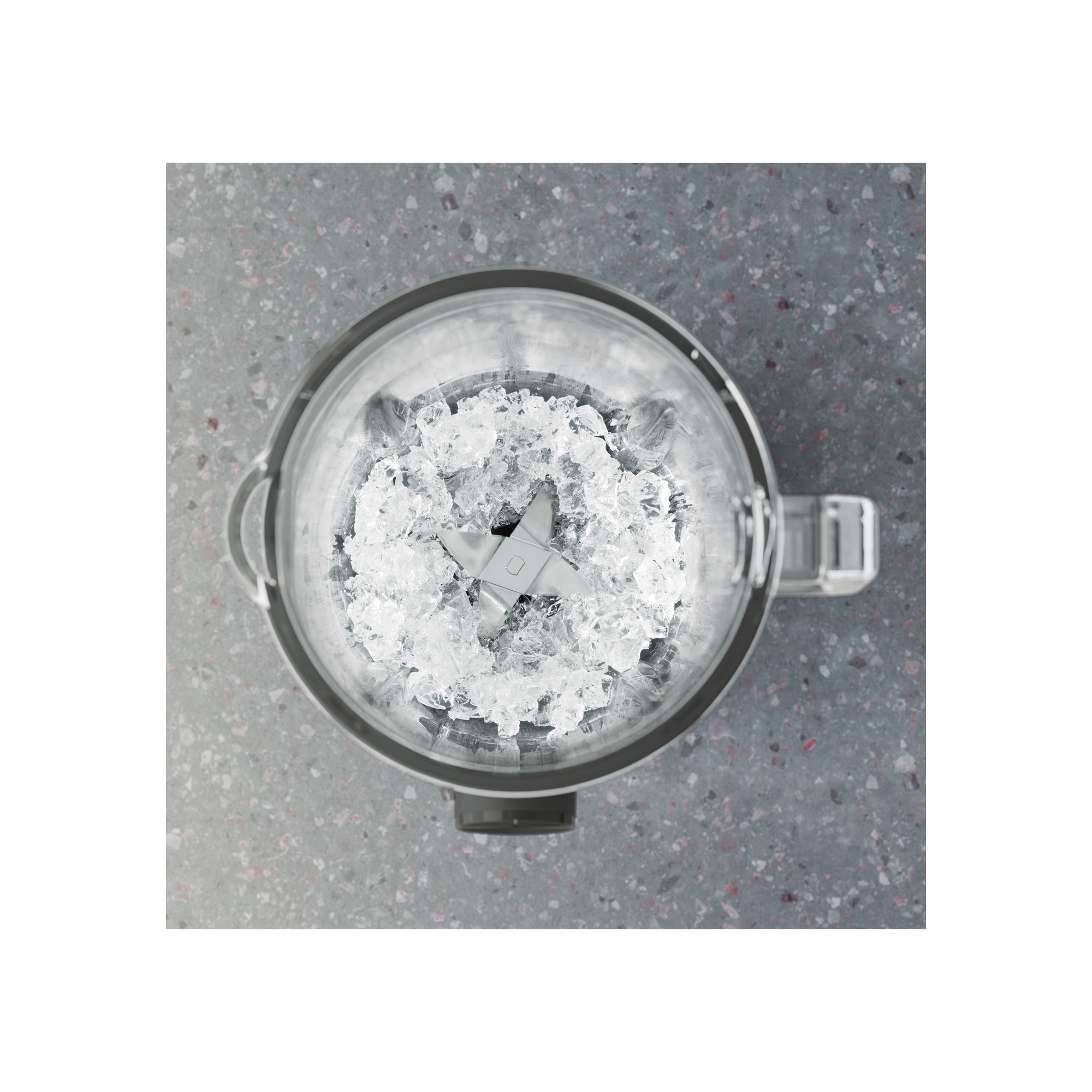 Benekli gri bir yüzey üzerinde buz küpleri ve bir bıçakla dolu bir blenderin yukarıdan görünümü.