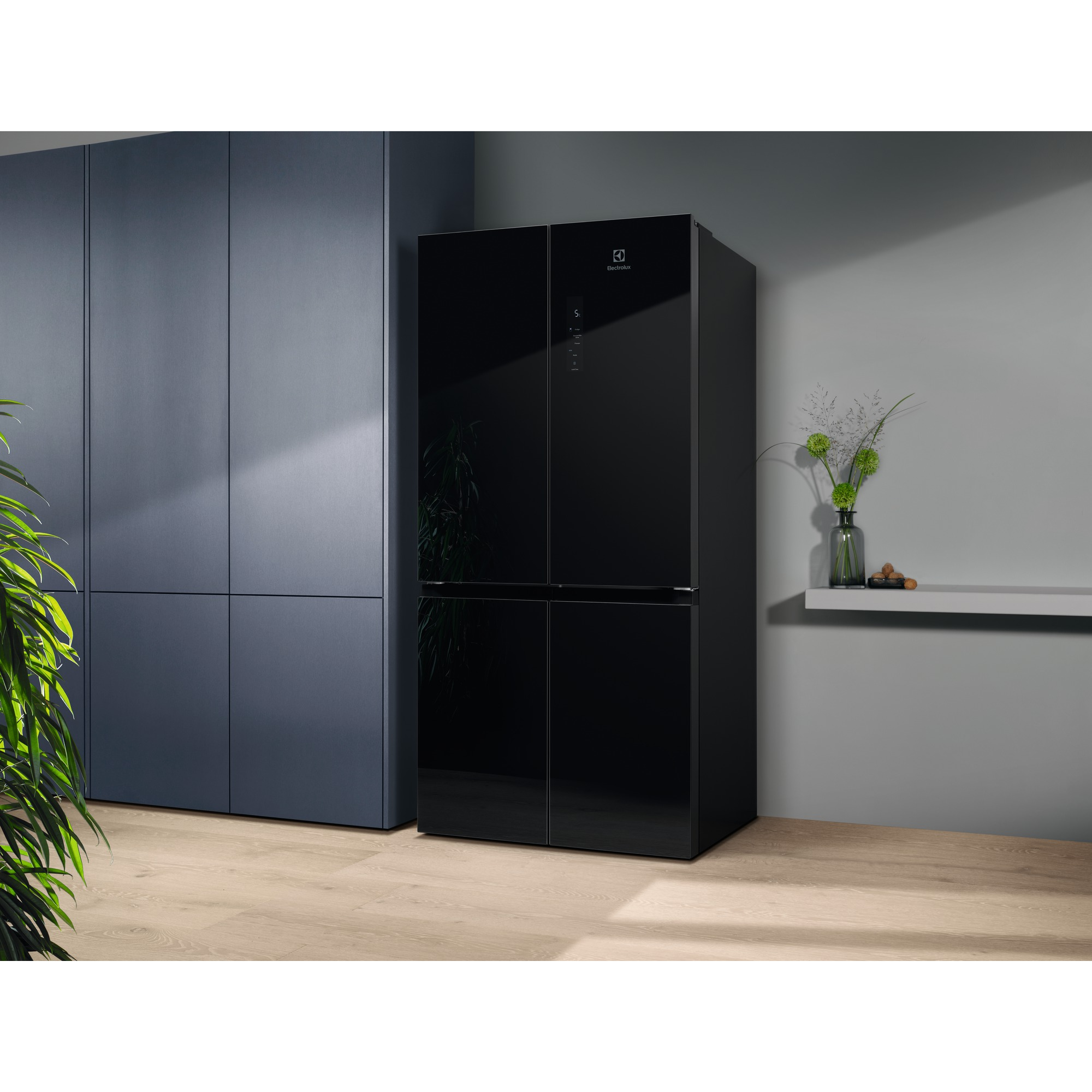 Siyah bir Electrolux buzdolabı, mavi dolaplar, gri duvarlar ve a çık renk ahşap zeminli bir odada duruyor. Dekorlu bir raf görülebilir.