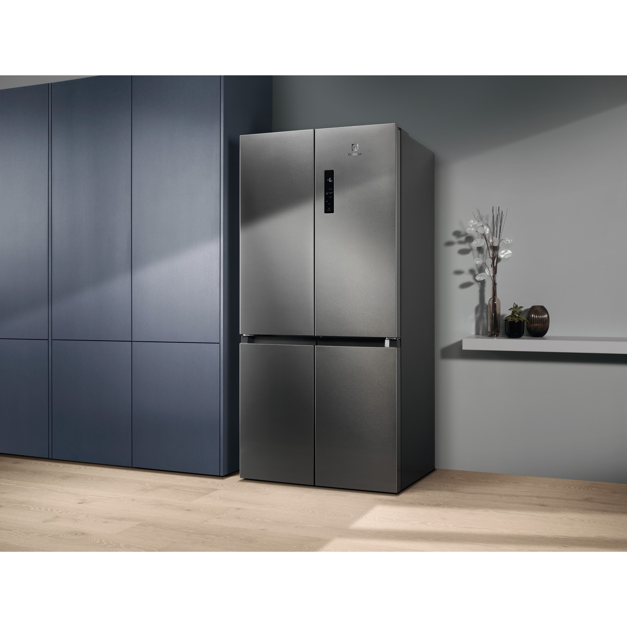 Paslanmaz çelik bir Electrolux buzdolabı, mavi dolaplar ve gri bir duvar bulunan bir odada duruyor. Bir raf dekorasyon tutuyor.