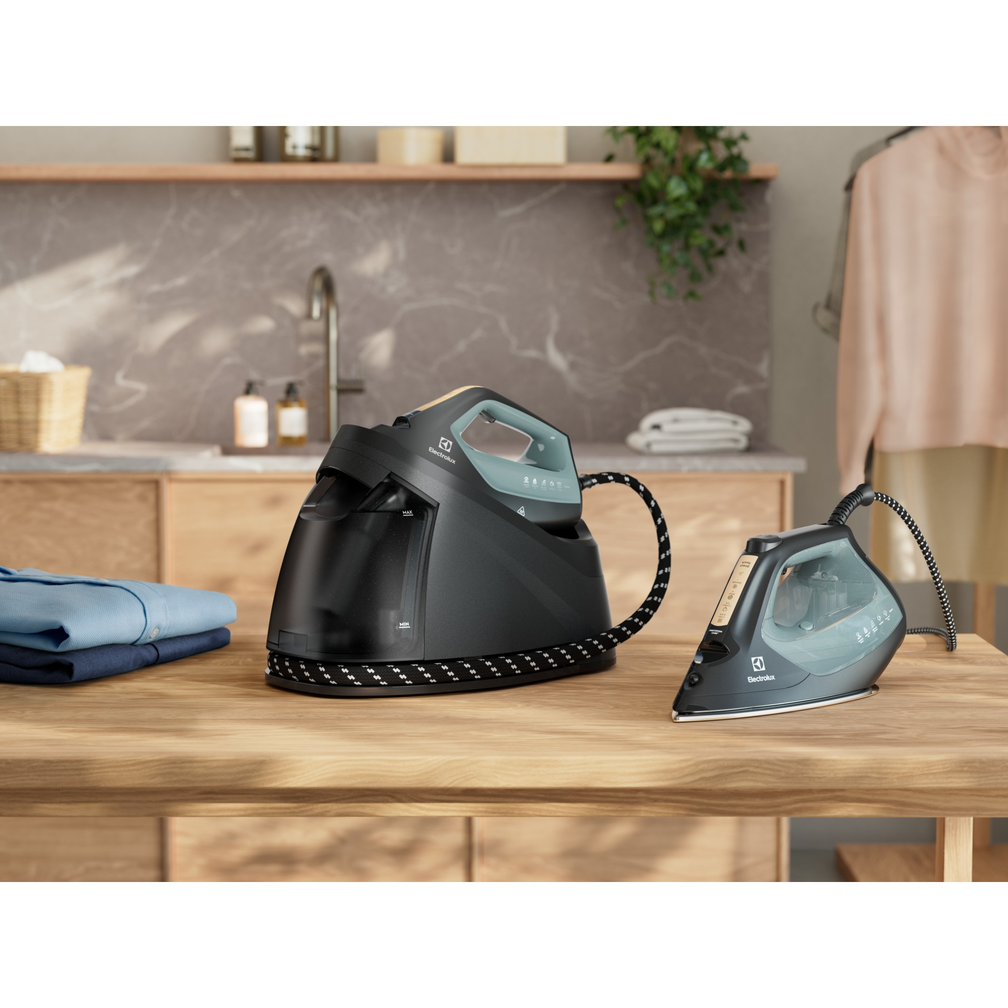 Ahşap bir masa üzerinde iki siyah Electrolux ütüsü. Solda bir yığın mavi gömlek. Çamaşırhane arka planı.