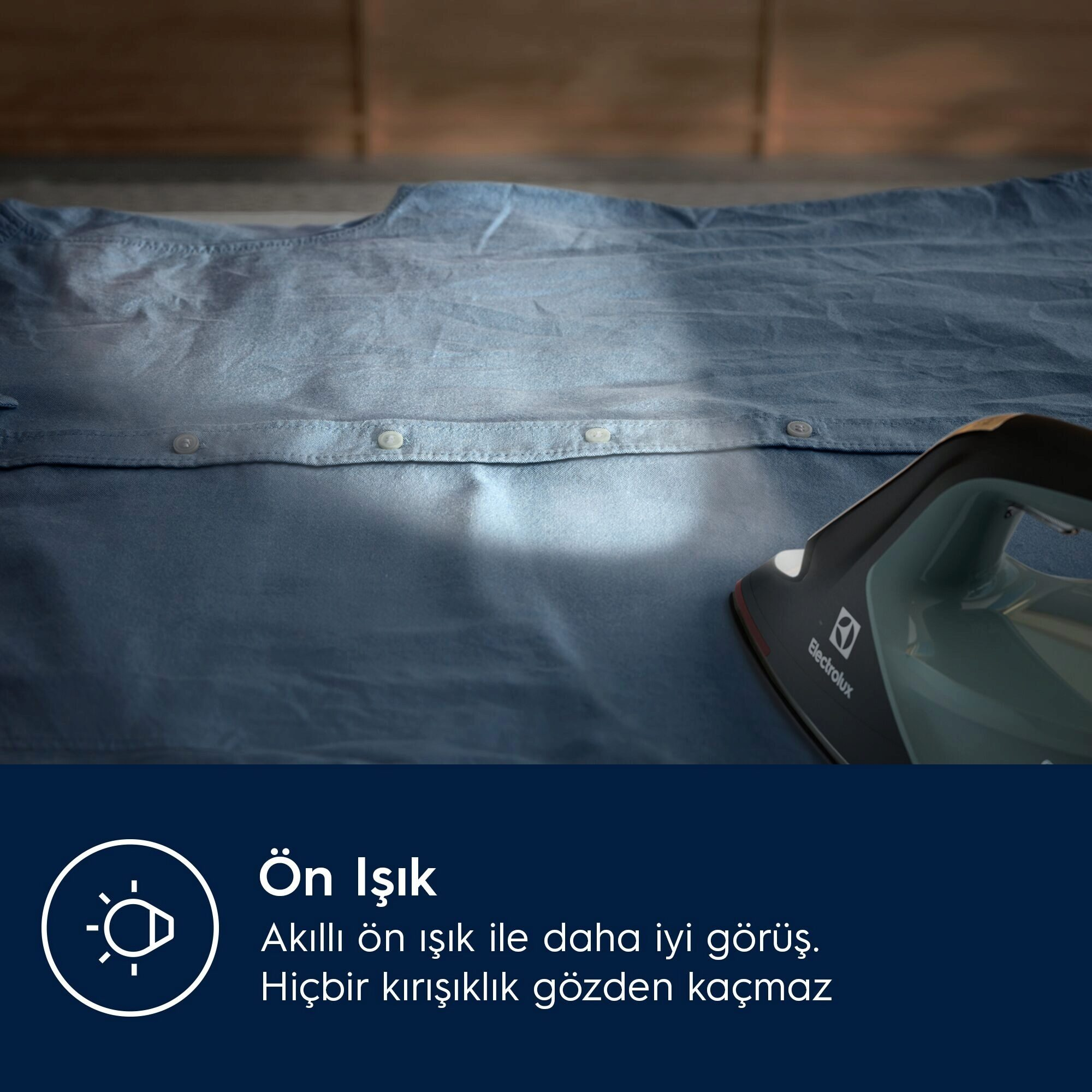 Mavi bir gömleğin üzerinde bir ütü. Ütü siyah ve gridir, Electrolux markasıdır. Gömleğin düğmeleri var.