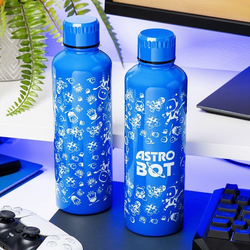 Két kék Astro Bot vizespalack az asztalon. Az egyiken a logó látható. Fehér rajzfilmfigurák borítják a palackokat. Egy vezérlő és egy billentyűzet látható.