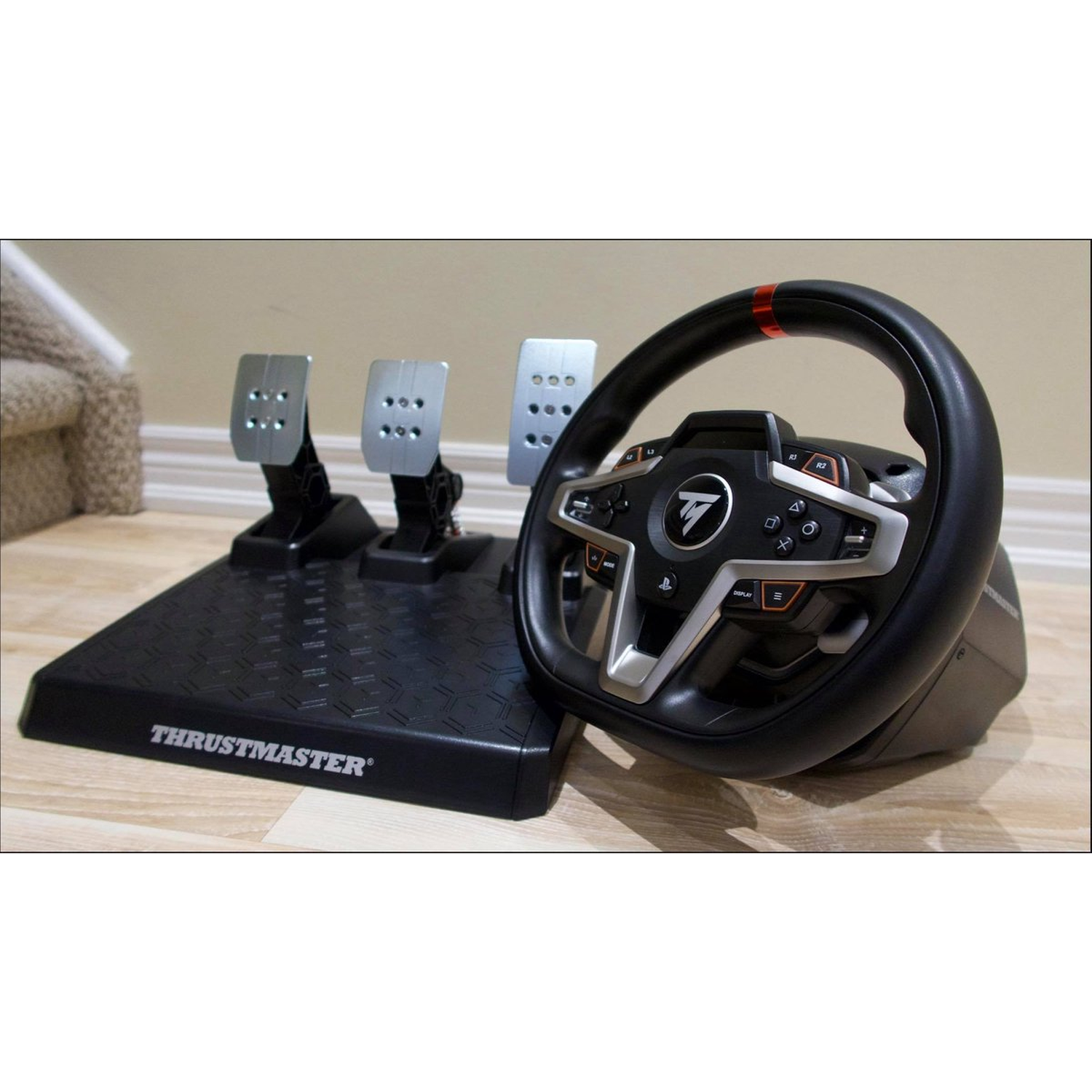 Een racestuur en pedaalset. Het stuur is zwart met zilveren accenten. Pedalen zijn zilver. De basis is zwart met Thrustmaster logo.
