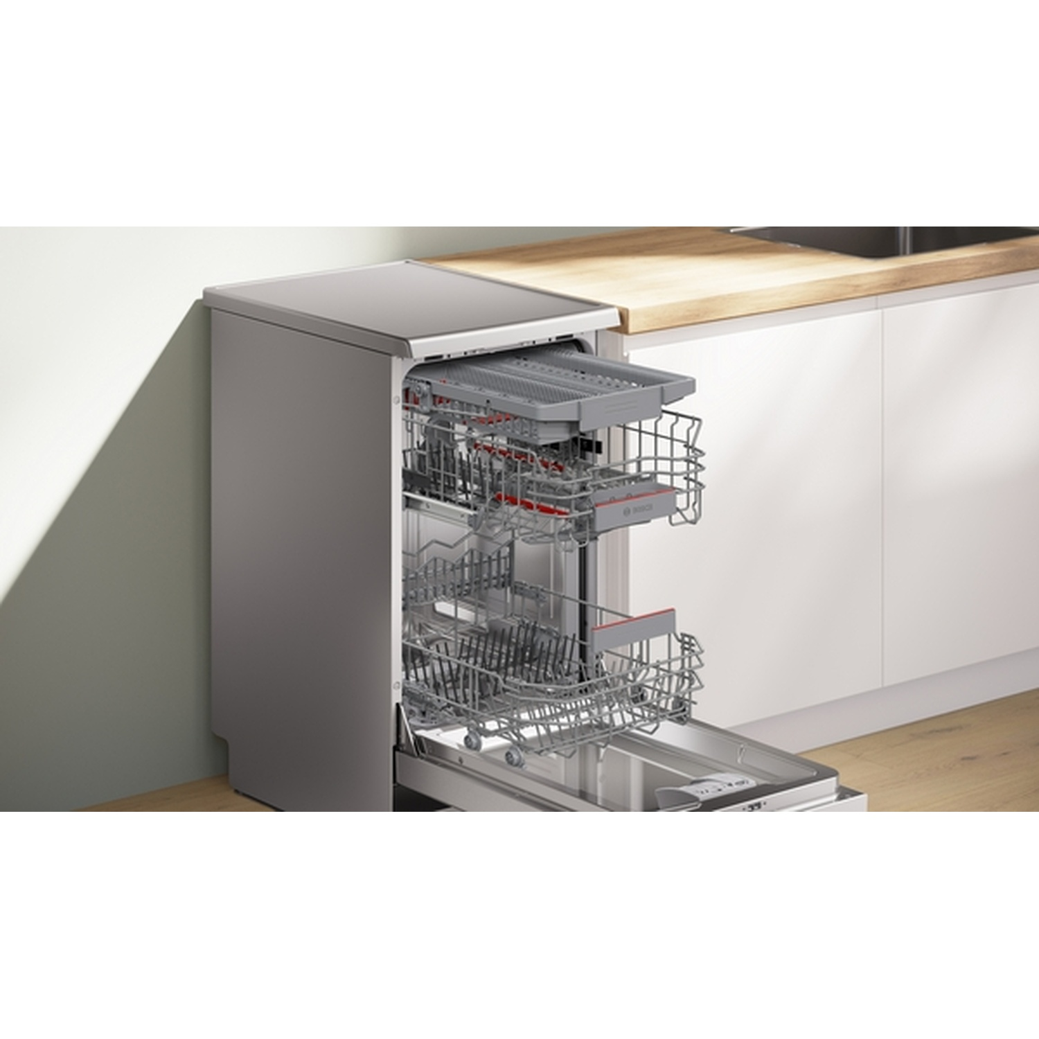Open dishwasher with racks visible. Silver exterior, interior with racks, red accents. Countertop and wall in background.