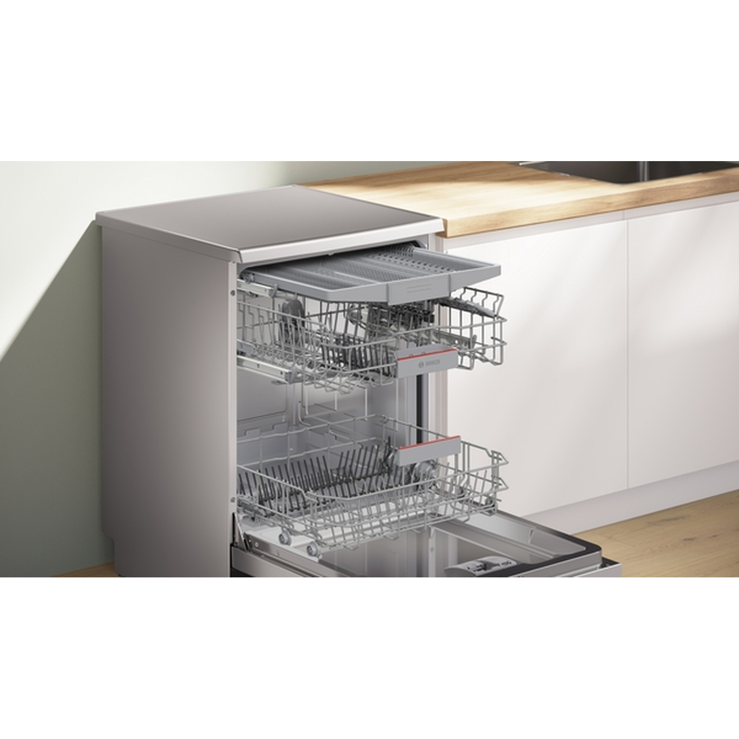 Open dishwasher showing racks. Stainless steel finish, with open door. Light wood countertop and white cabinets are visible.