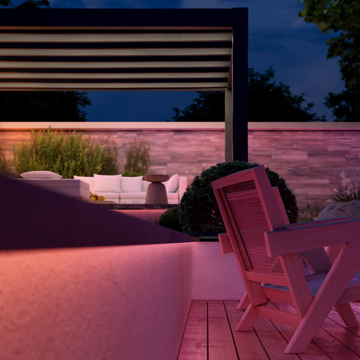 Außenszene bei Nacht. Holzstühle, weißes Sofa und ein Tisch stehen unter einem Baldachin. Rosa Umgebungslicht beleuchtet die Szene.