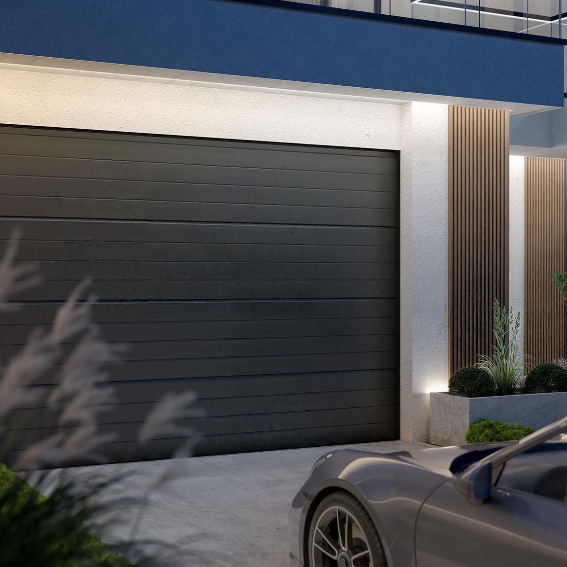 Eine moderne Garage mit dunkler grauer Tür und einem grauen Sportwagen davor. Das Gebäude hat Holzakzente und Grün.