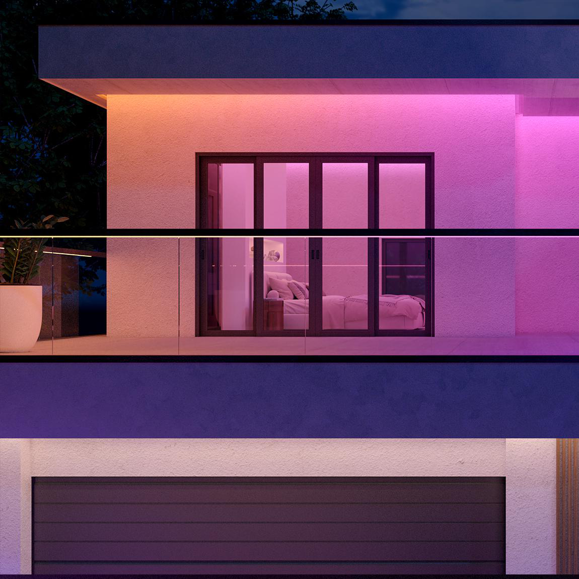Modernes Haus von außen bei Nacht. Schlafzimmer mit Bett durch Glastüren sichtbar. Bunte Lichter beleuchten die Fassade.
