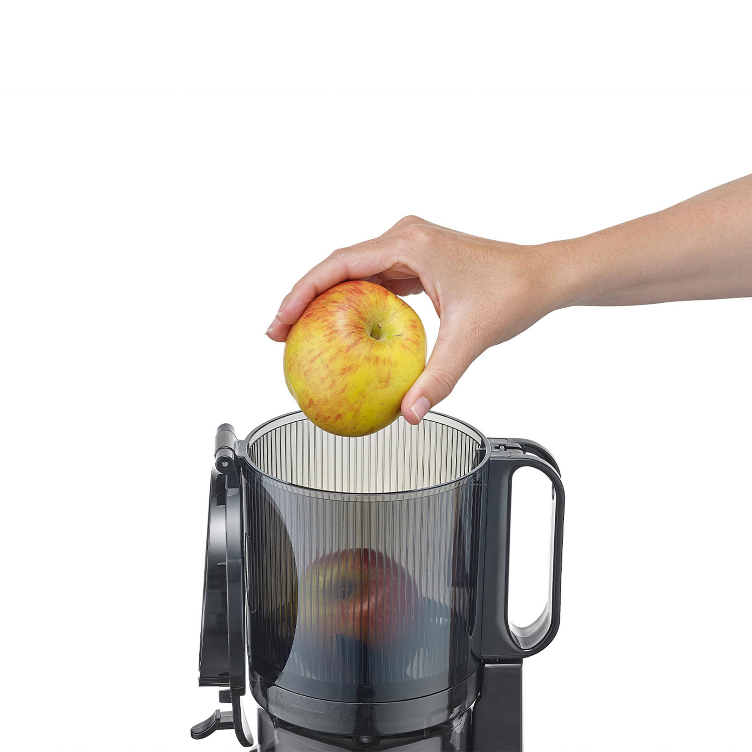 Eine Hand legt einen gelb-roten Apfel in einen schwarzen Entsafter. Ein weiterer Apfel befindet sich im Entsafter.