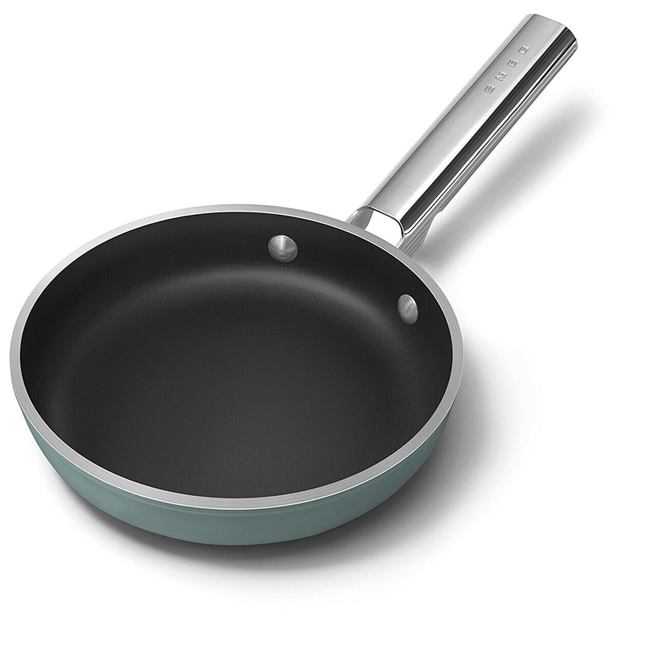 Eine türkisfarbene Bratpfanne mit schwarzem Innenraum und silberfarbenem Griff, die auf einer weißen Oberfläche steht. Auf dem Griff steht SMEG.