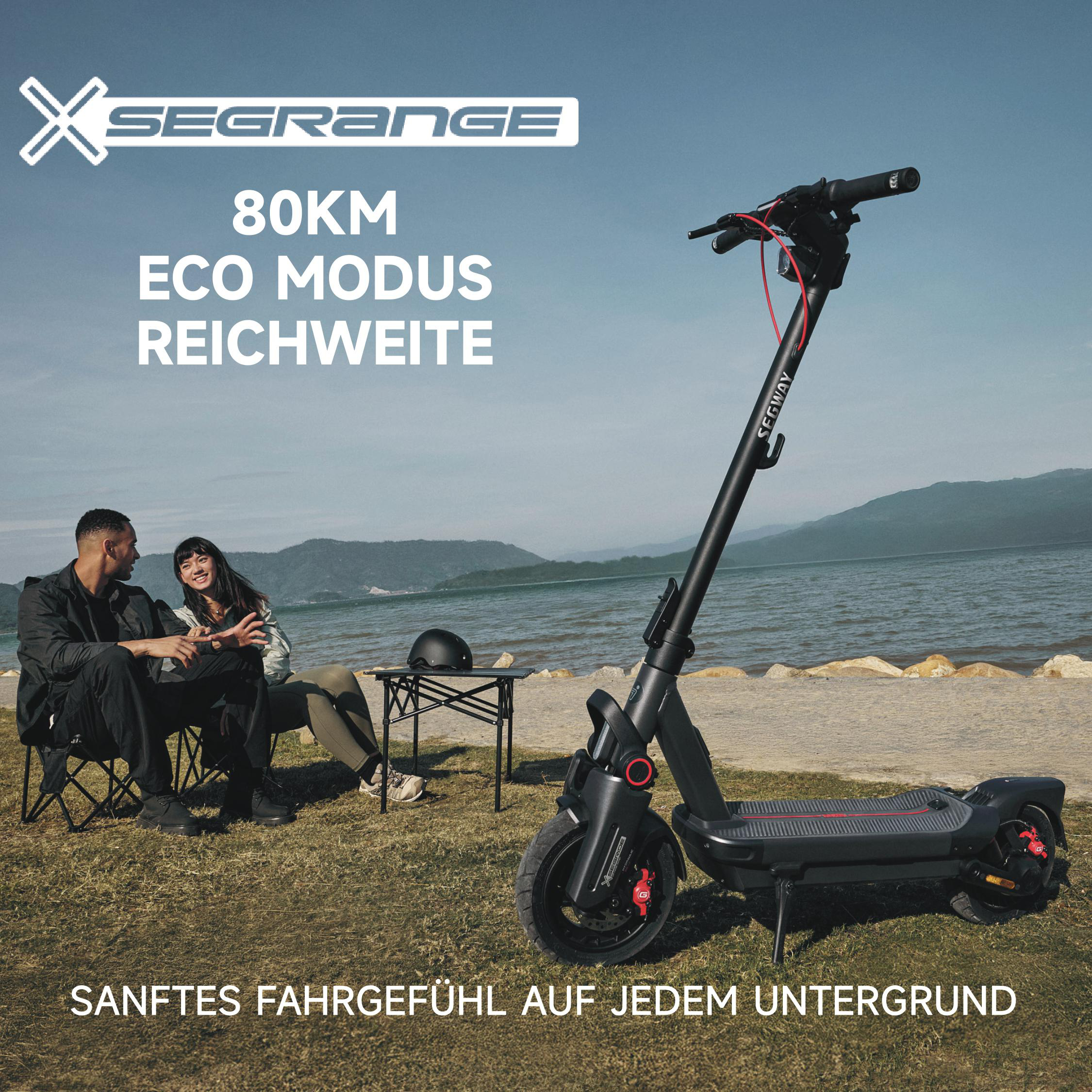 Ein schwarzer Segway-Roller steht neben einem Paar, das auf dem Rasen sitzt. Im Hintergrund sind See und Berge zu sehen.