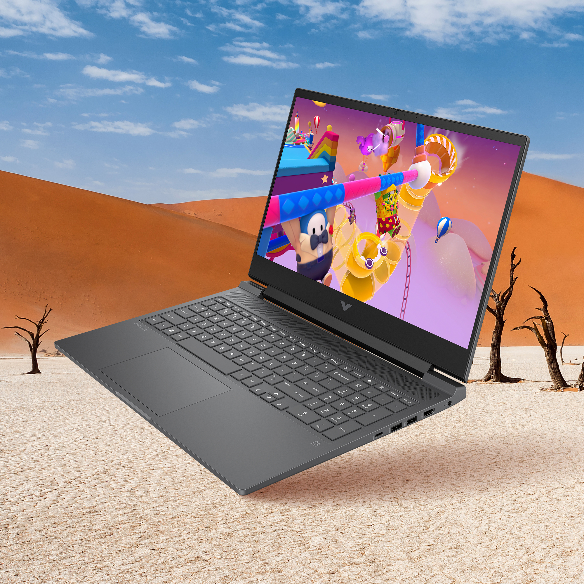 Laptop z grą w krajobrazie pustynnym. Laptop jest otwarty, wyświetlając kolorowy ekran gry.