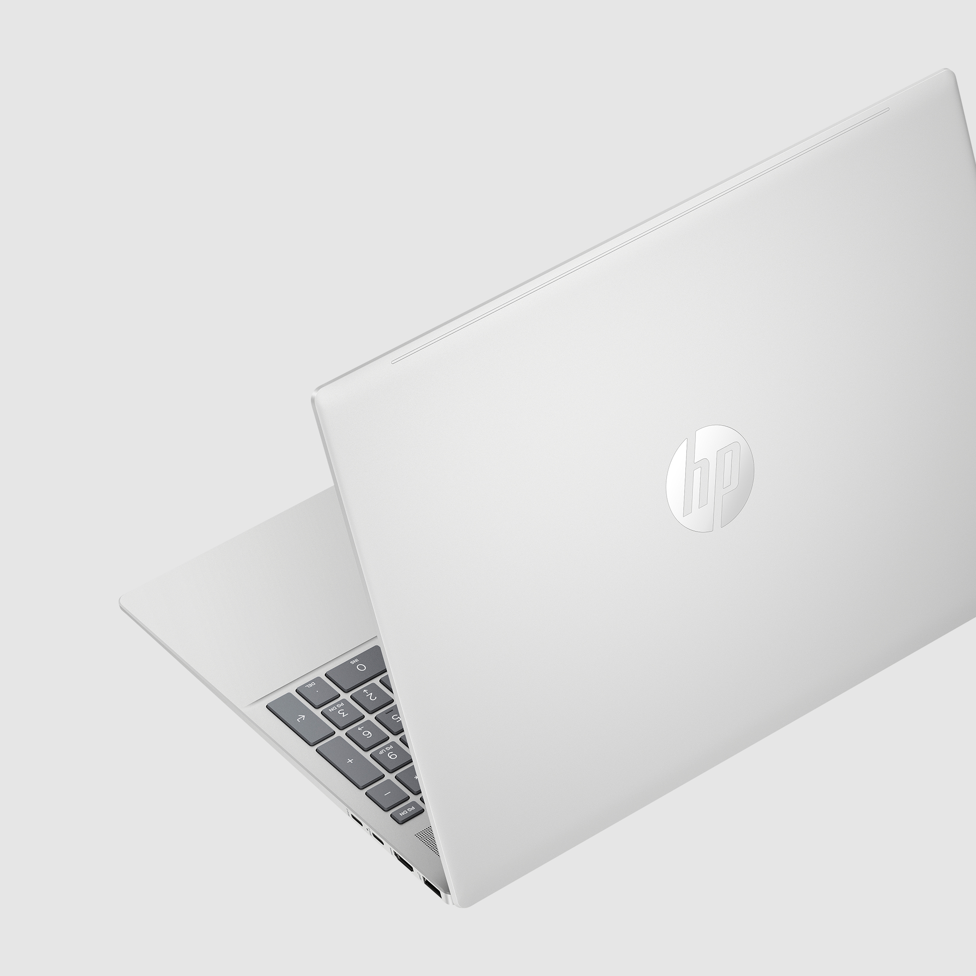 Biały laptop HP jest częściowo otwarty, pokazując klawiaturę i tył z logo HP na szarym tle.
