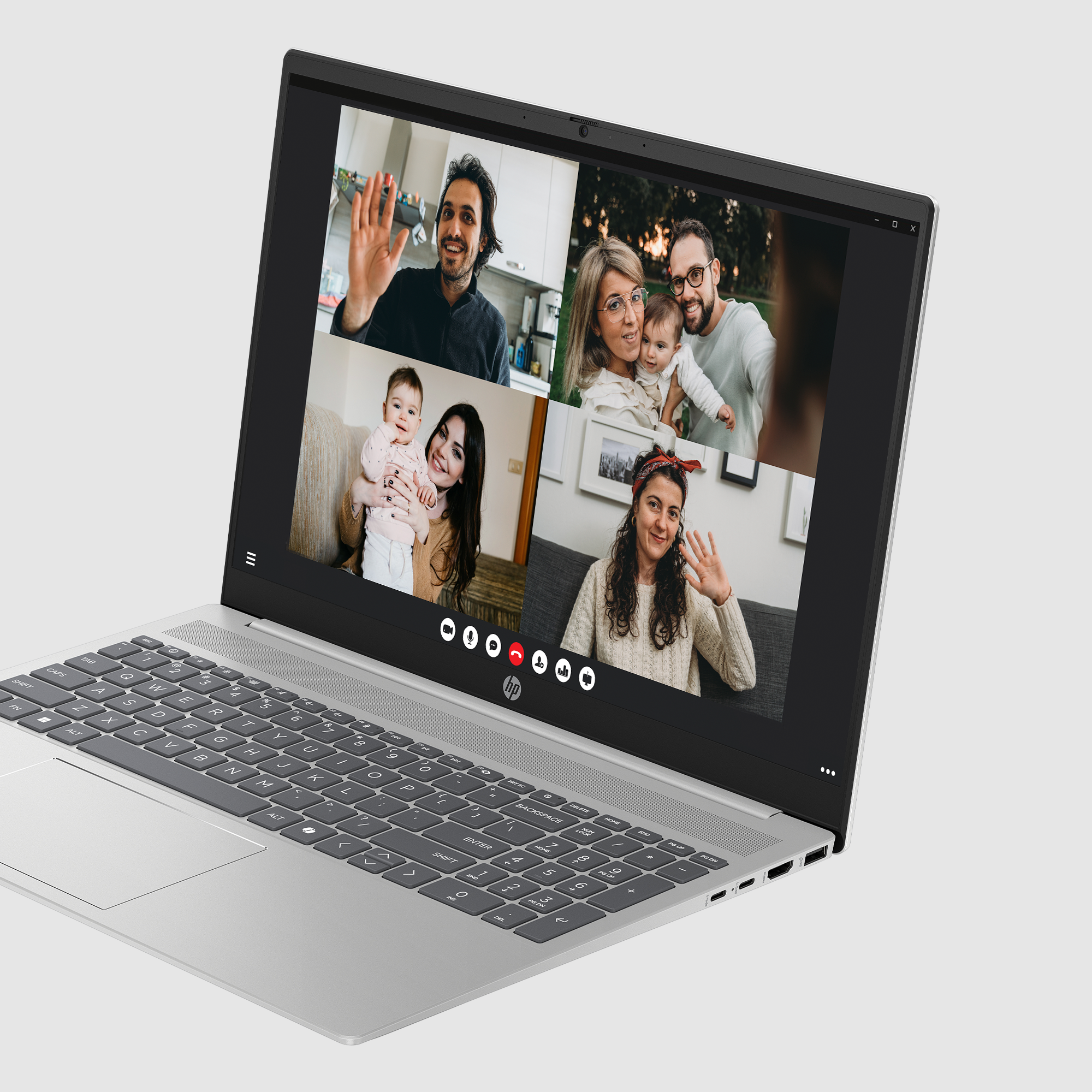 Ekran laptopa pokazuje rozmowę wideo z czterema rodzinami. Ludzie machają. Laptop jest otwarty na jasnoszarej powierzchni.