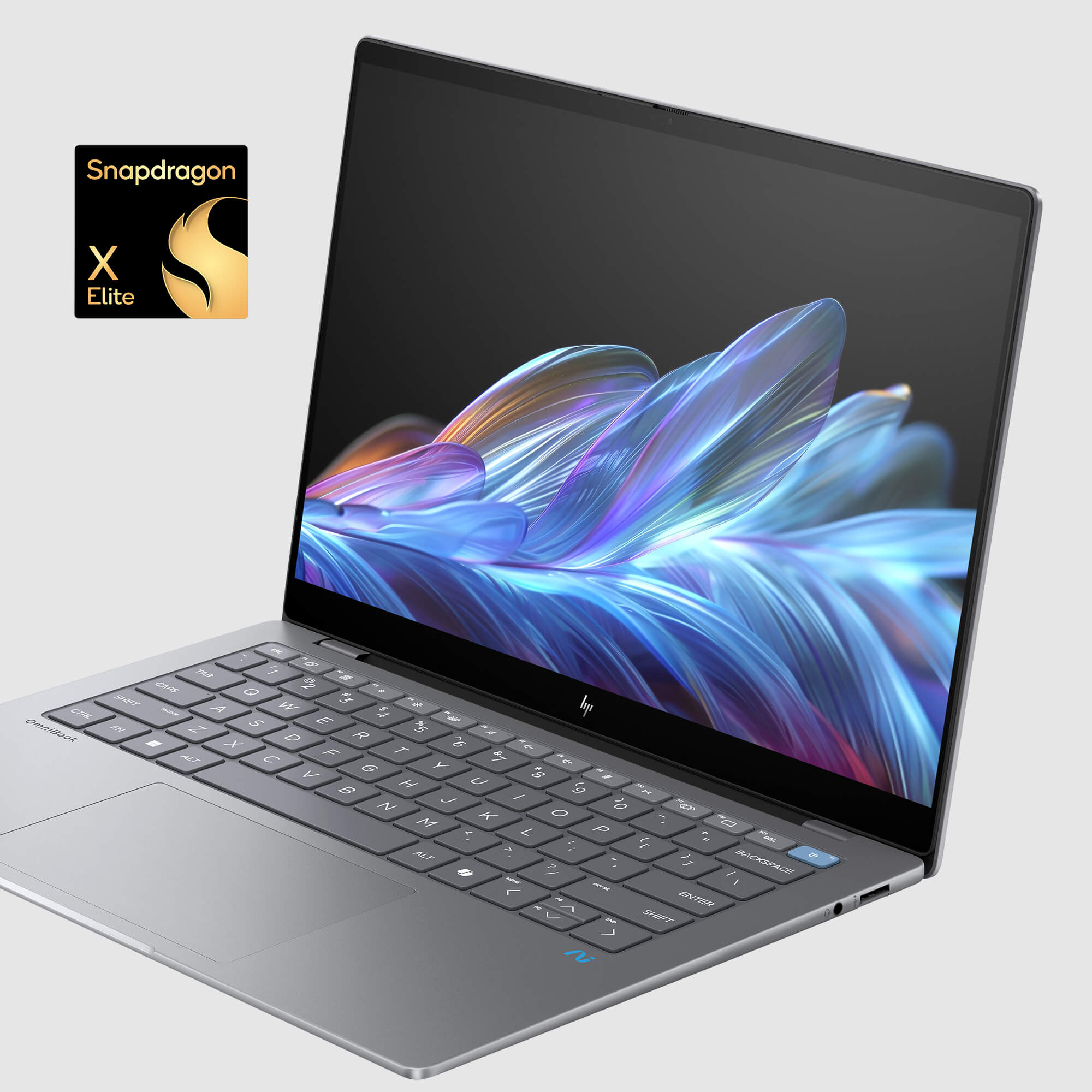 Srebrny laptop z otwartym ekranem wyświetlającym kolorową sztukę abstrakcyjną. Klawiatura jest widoczna, a logo Snapdragon X Elite jest u góry.