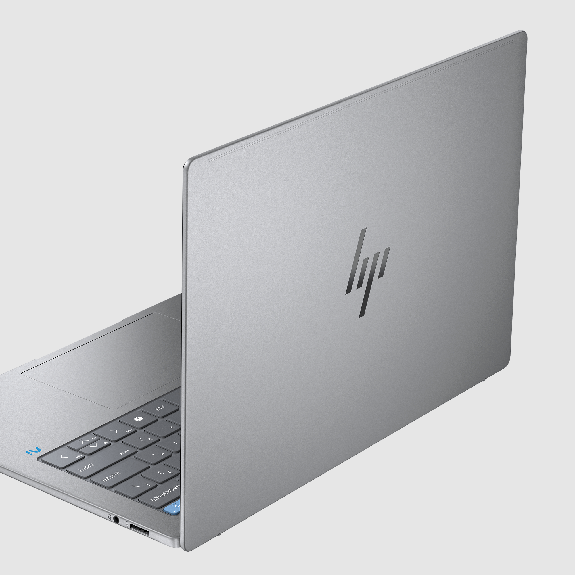Srebrny laptop, lekko otwarty, pokazujący klawiaturę i logo HP. Tło jest białe.