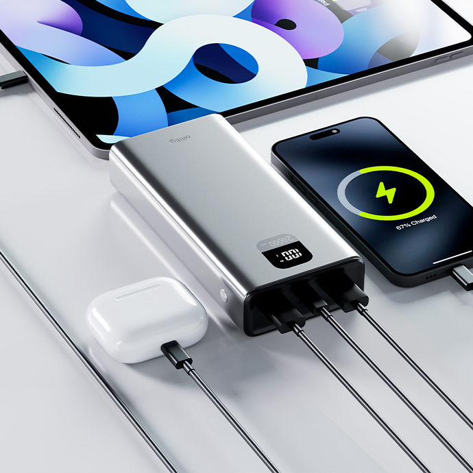 Ezüst power bank tölt egy iPad-et, telefont (67% töltöttség) és AirPods-t. Kábelek be vannak dugva. Fehér háttér.