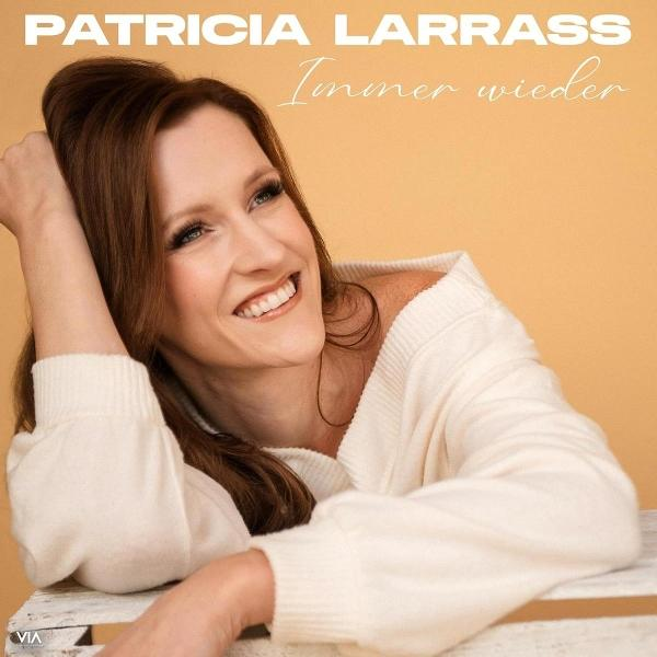 Frau lächelt, trägt einen weißen Pullover, hat braune Haare und lehnt sich auf einer Oberfläche. Text oben: 'PATRICIA LARRASS' und 'Immer wieder'.