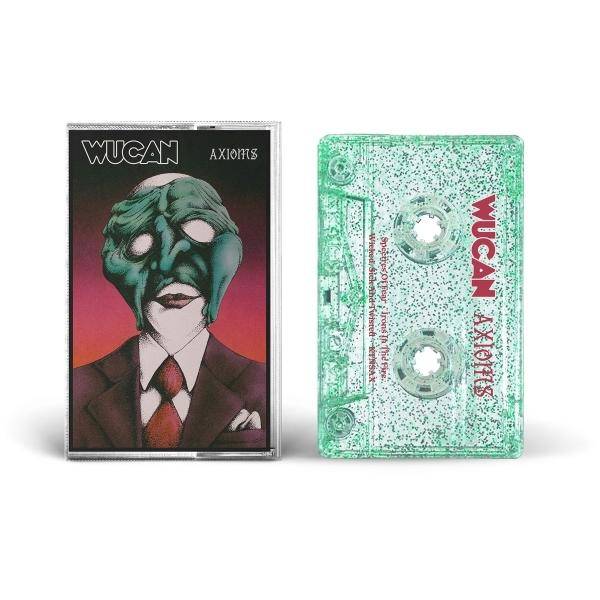 Eine Kassette mit grünem Gesicht und einer Hülle mit einer surrealen Gesichtsillustration auf lila Hintergrund.