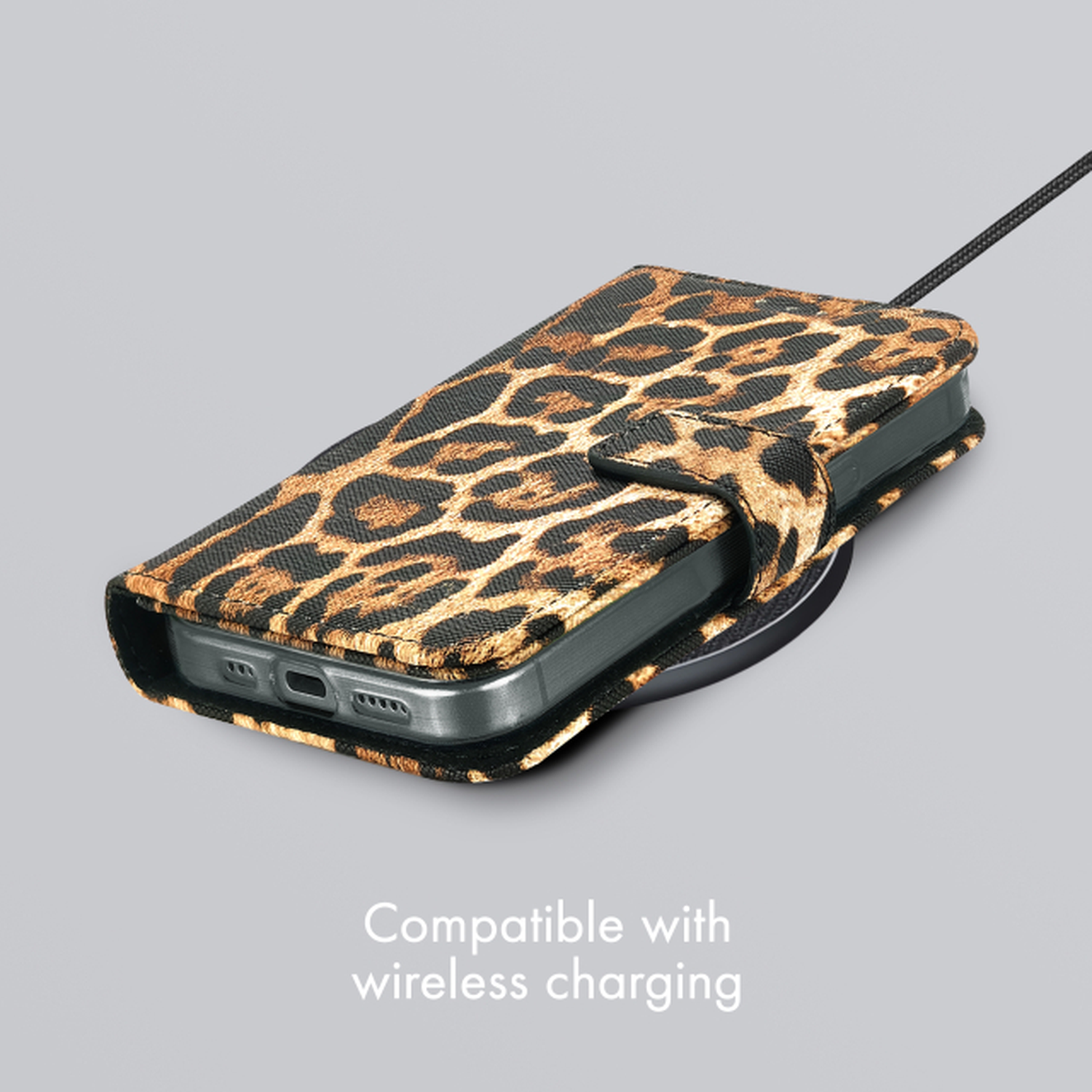 Étui de téléphone à imprimé léopard sur un chargeur sans fil. Câble noir connecté. Fond gris.