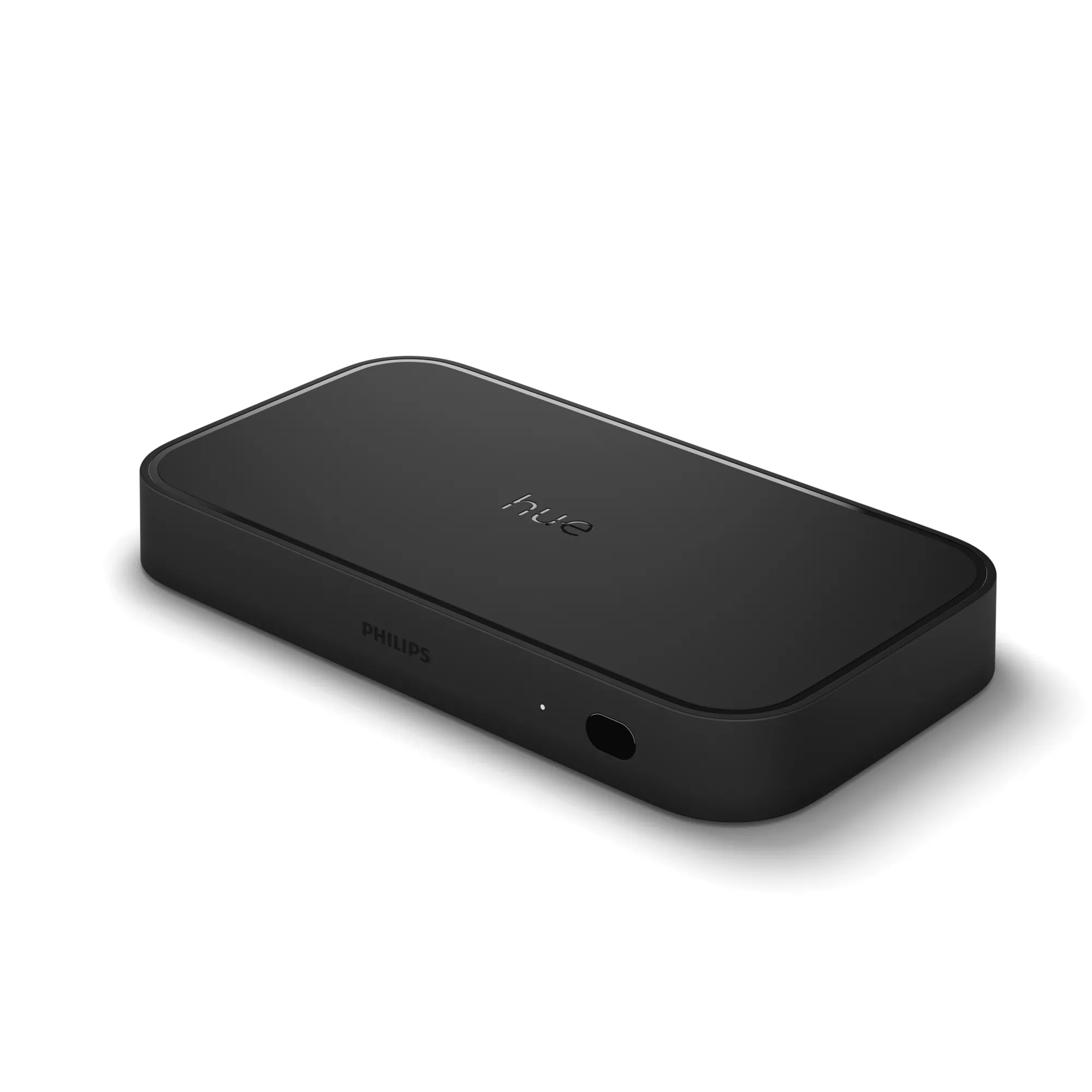 Un puente Philips Hue negro sobre una superficie blanca. El dispositivo tiene la palabra 'hue' y 'Philips'.