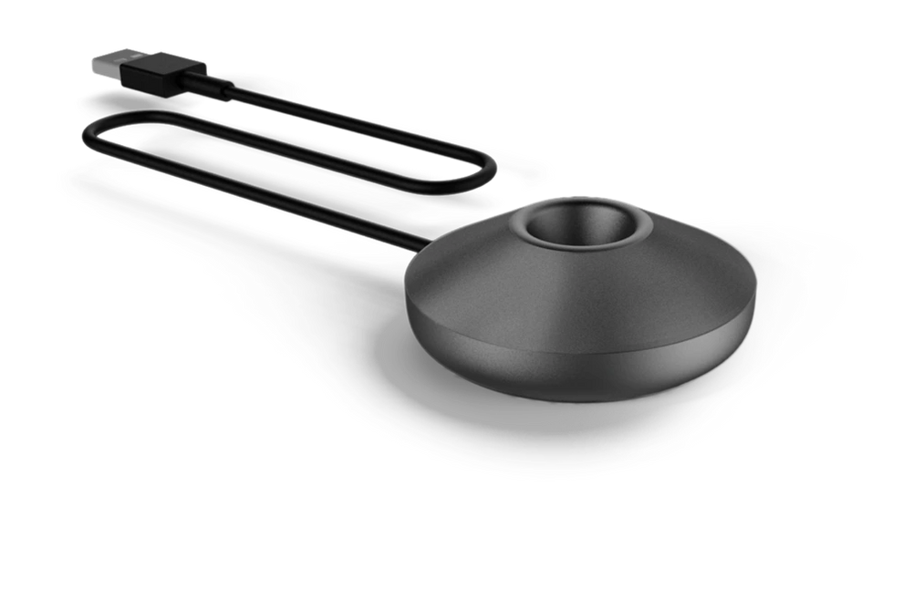 Egy fekete töltőállomás, kerek alappal és egy lyukkal a tetején. Egy fekete USB kábel csatlakozik az állomáshoz.