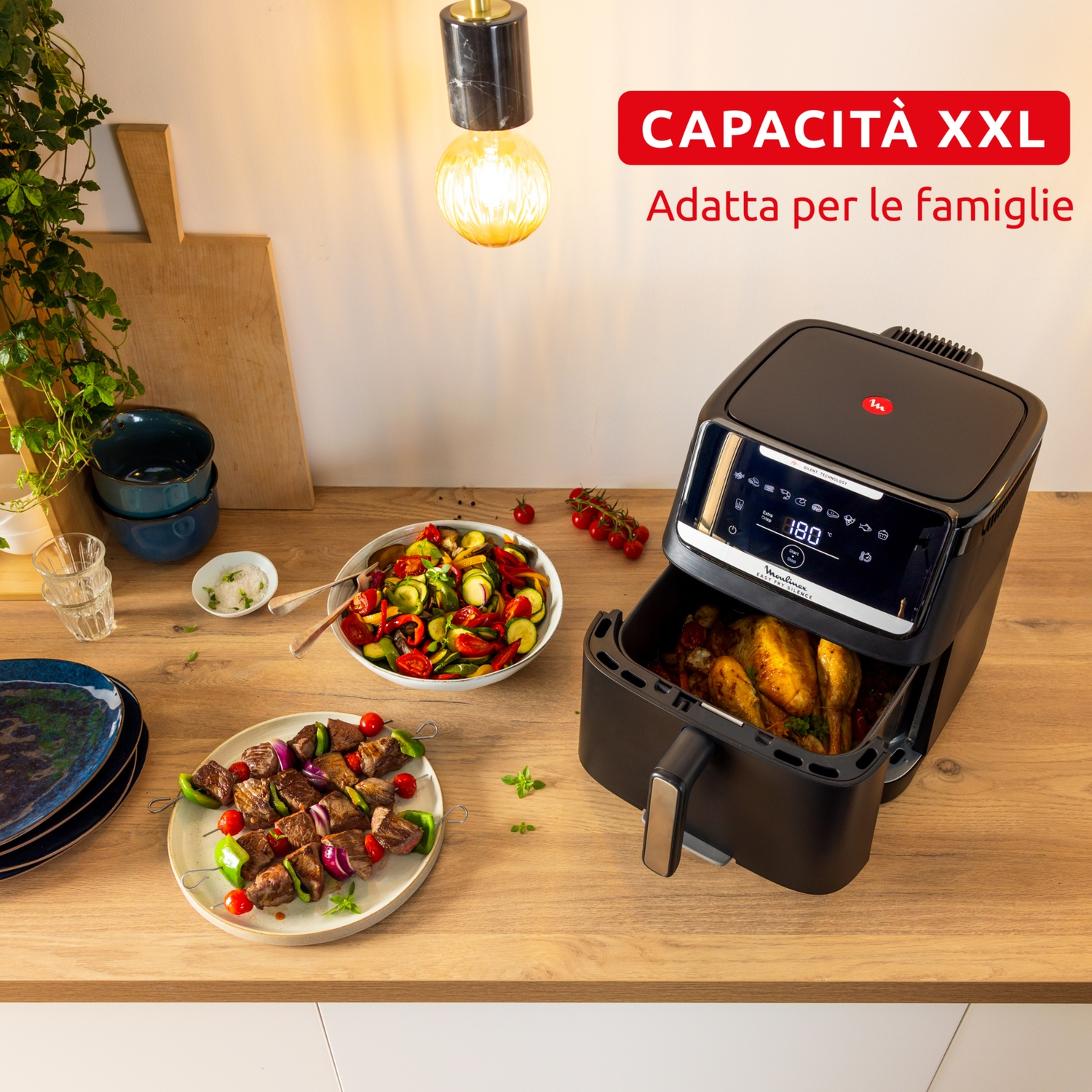 Una friggitrice ad aria con cibo dentro, un piatto con spiedini, una ciotola di verdure e altri piatti su un tavolo di legno.